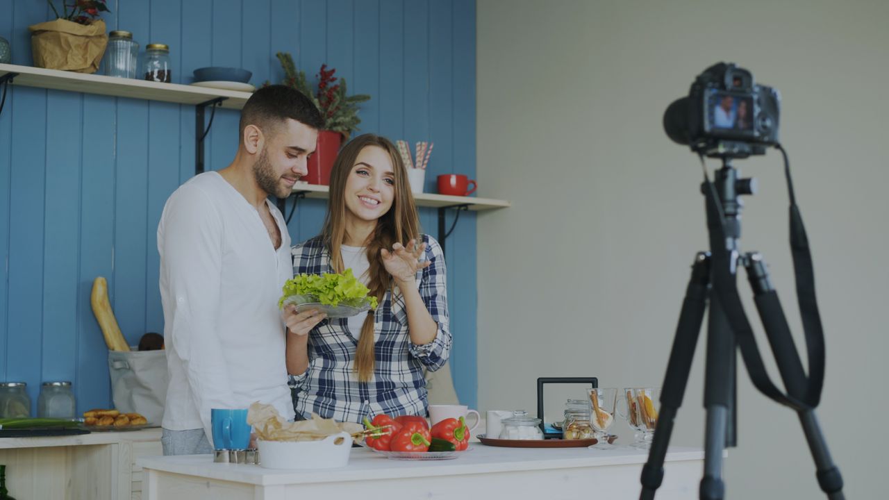 A couple filming a cooking video, showcasing fresh ingredients in a cozy kitchen setting.