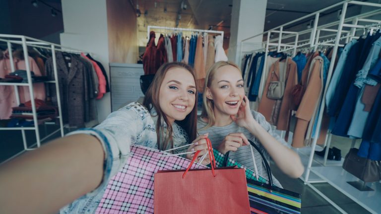 Two women happily shopping with bags in a fashionable clothing store.